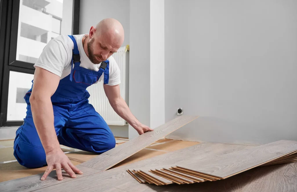 Man in workwear installing laminate flooring, showcasing our Interior house painting service and Flooring Installation expertise.