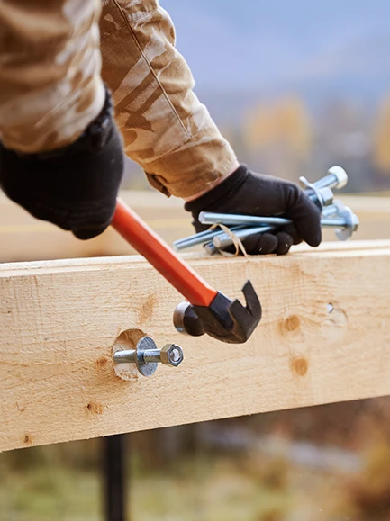 Worker tightening a bolt with a wrench on a wooden beam during deck construction.
