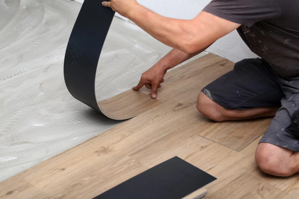 Worker installing new vinyl tile floor as part of flooring installation services and home improvement.