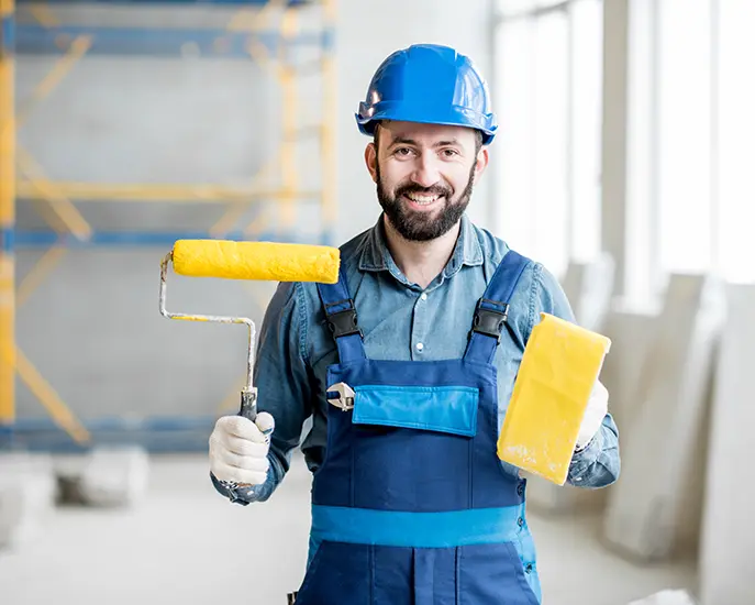 Smiling painter holding a paint roller and tray during a commercial painting project.