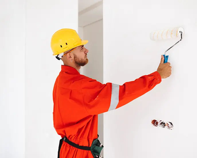 Worker in protective gear painting a white wall with a roller during a commercial painting project.