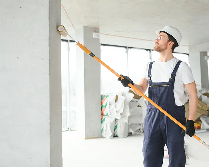 Painter using a roller to apply paint to a concrete wall during a commercial painting project.