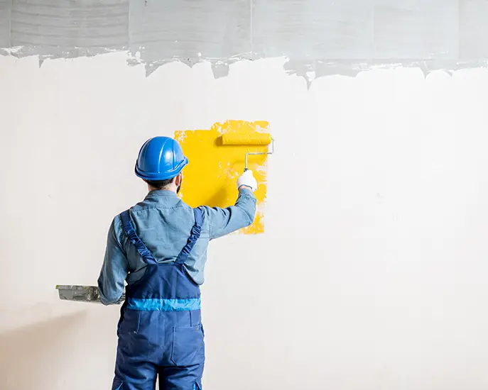 Construction worker painting a wall with yellow paint during a commercial painting project.