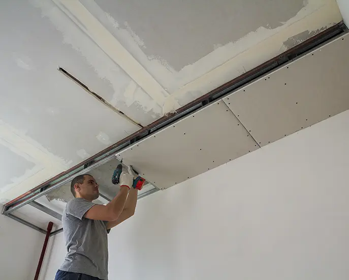 Professional drywall installer securing ceiling drywall panels with a power drill.