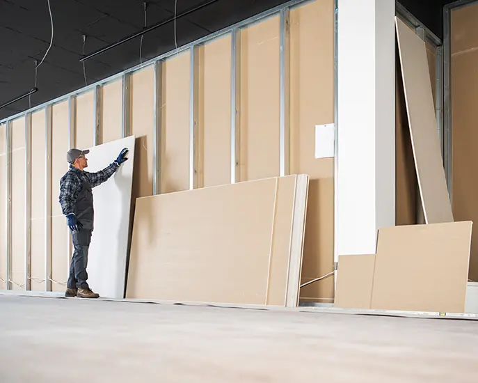 Worker preparing drywall panels for installation on a metal stud frame in a construction project.
