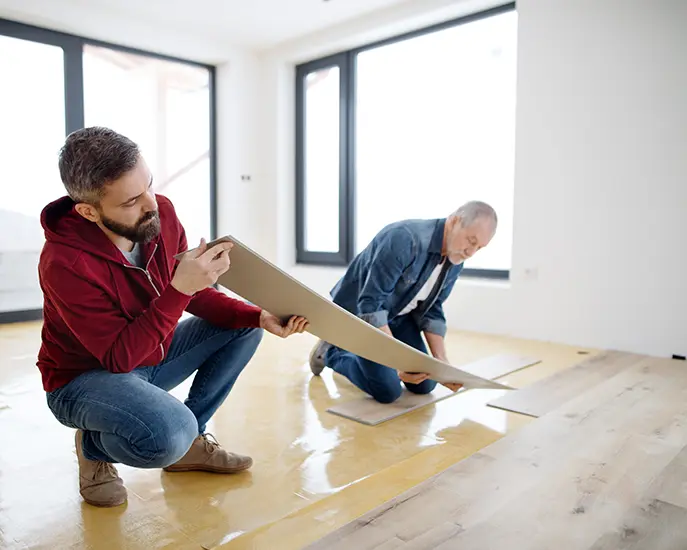 Two flooring experts installing laminate floor panels in a modern home.