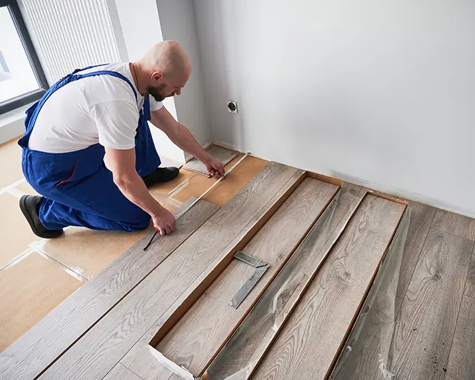 Professional worker in blue overalls installing hardwood flooring in a residential space.