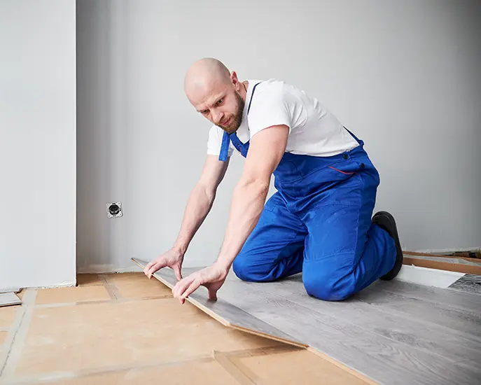 Skilled worker in blue overalls installing laminate flooring in a home renovation project.