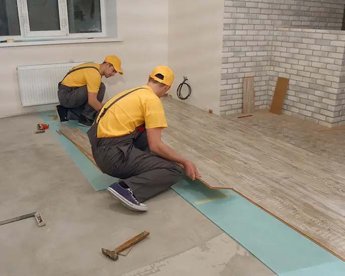 Two professional installers fitting wooden laminate flooring during a home renovation.