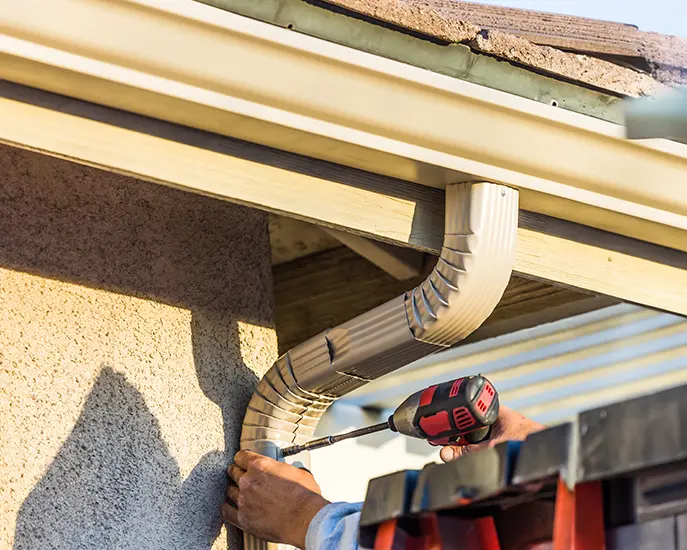 Worker securing a gutter downspout during a gutter installation project.