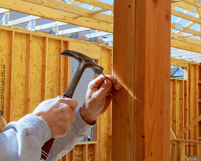 Close-up of a worker hammering a nail into a wooden frame during a home addition project.