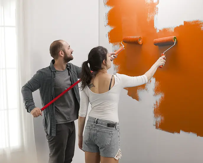 Couple painting a wall orange together during a home renovation project.