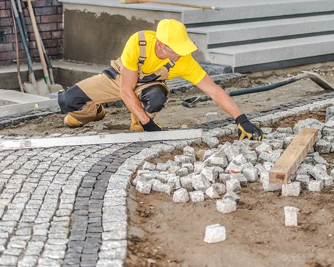 Worker installing stone pavers for a curved pathway during a stone installation project.