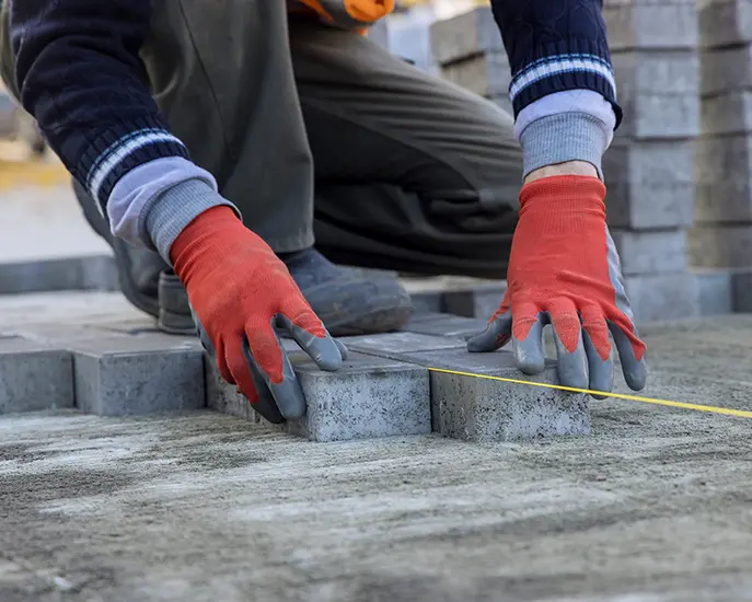 Worker aligning stone pavers with a string line during a stone installation project.