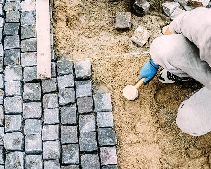 Worker laying stone pavers during a stone installation project.