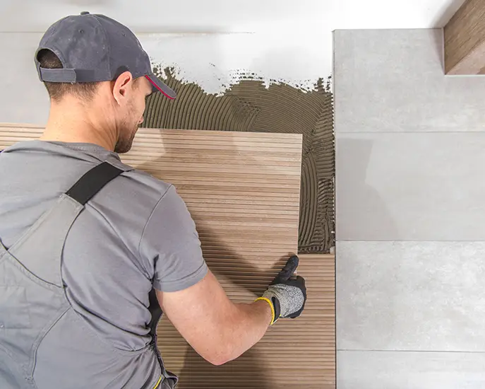 Worker laying large ceramic tiles on the floor during a tile installation project.