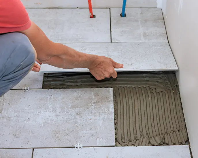 Worker installing floor tiles with adhesive during a tile installation project.