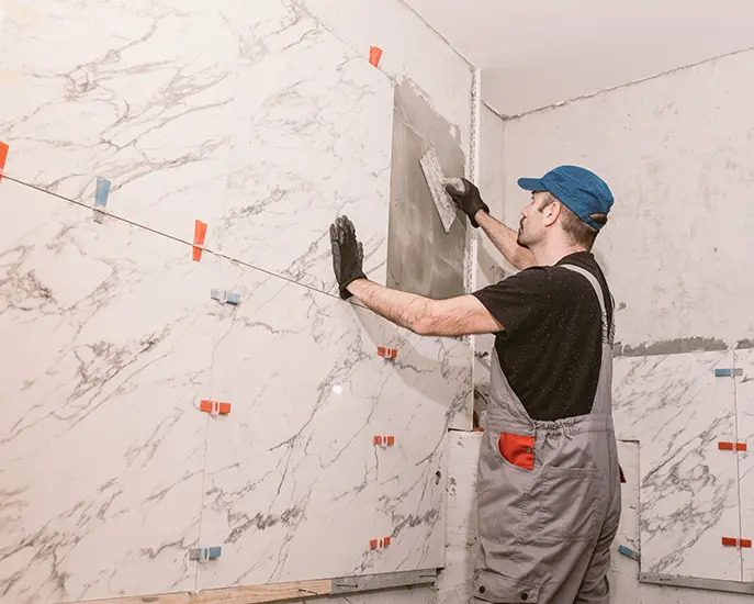 Worker installing marble tiles on a bathroom wall during a tile installation project.