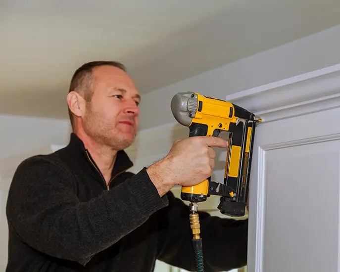 Contractor installing crown molding with a pneumatic nail gun.