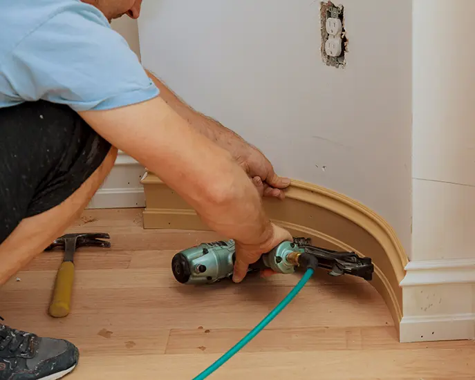 Contractor installing curved baseboard molding with a pneumatic nail gun.