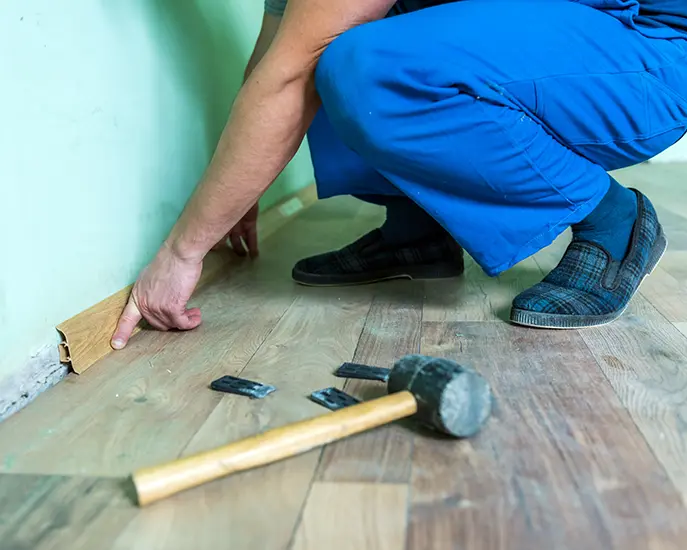 Carpenter installing floor trim molding with a hammer for a precise finish.