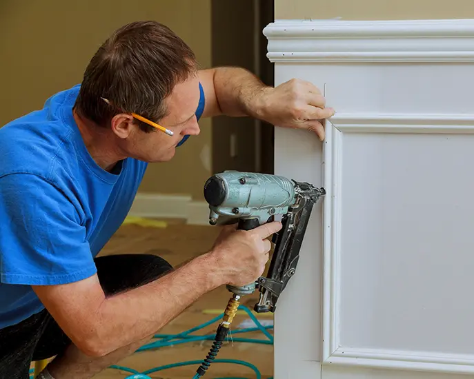 Professional carpenter installing trim molding using a nail gun for precision work.