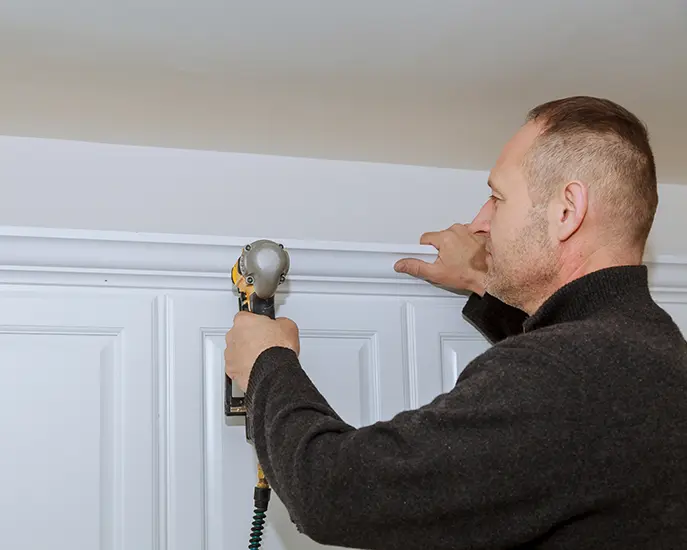 Professional installing crown molding with a nail gun, ensuring precision and a seamless finish.