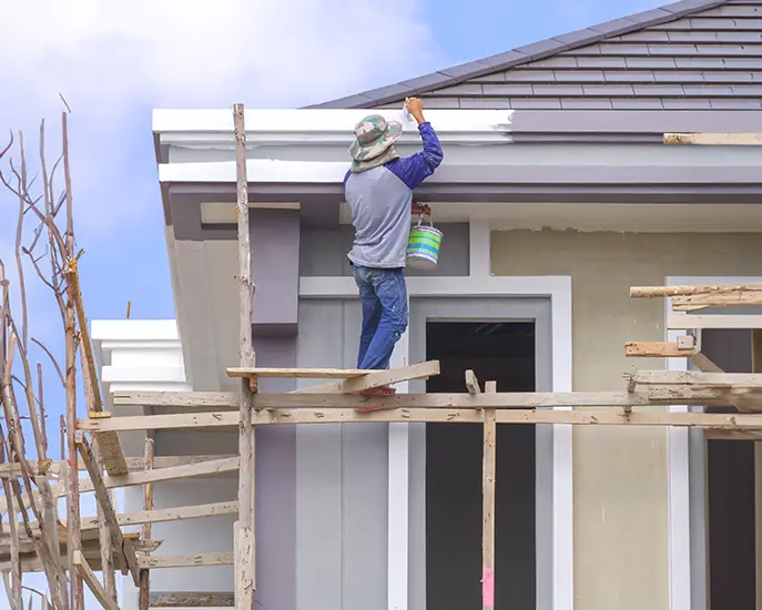 Worker painting the exterior of a house on scaffolding.