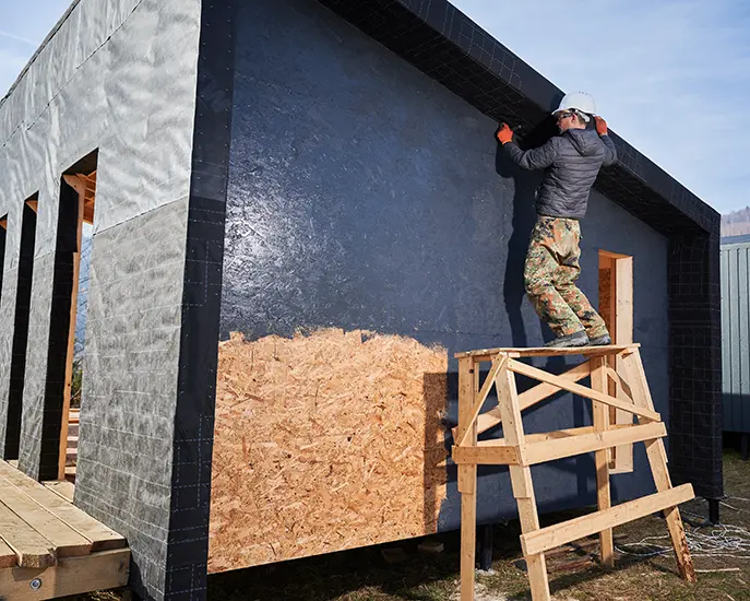 Worker applying exterior paint on a new construction home using scaffolding.