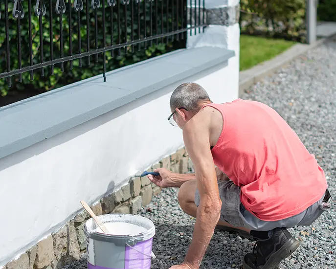 Contractor applying white paint to an exterior wall with a paintbrush.
