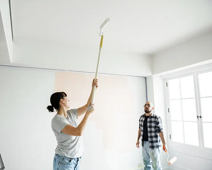 Man and woman painting a white ceiling and wall during a home renovation.